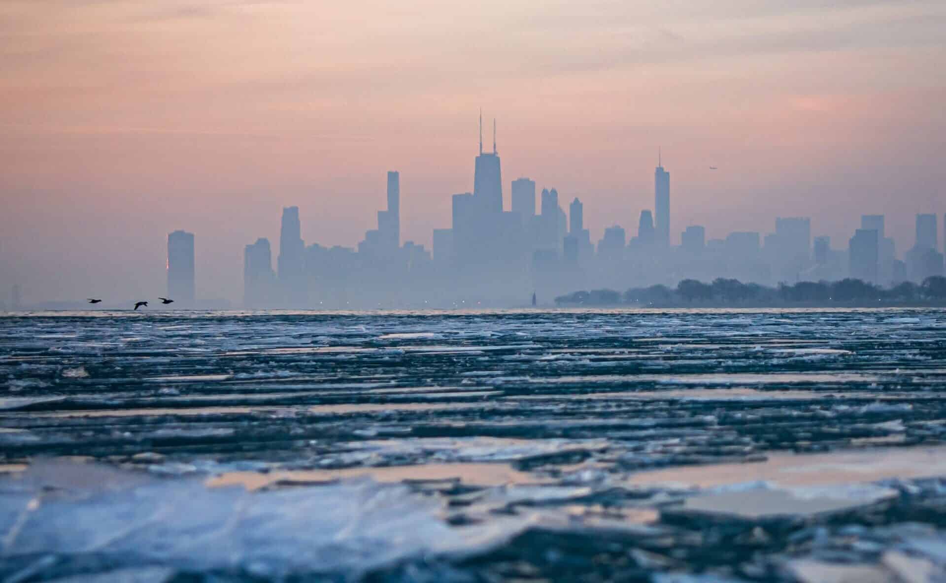 A photo of the chilly Lake Michigan in the winter is silhouetted by the Chicago skyline.