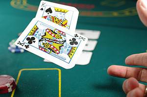 A hand flips two cards onto a green table in a gambling context