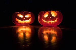 Two jack-o-lanterns lighted up against a black background