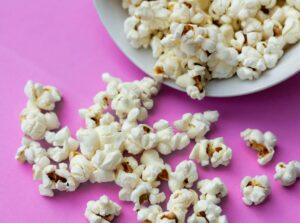 popcorn in a white bowl with some spilled over on a pink background