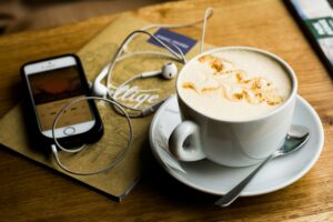 Table with a coffee cup and wired earbuds connected to a phone.